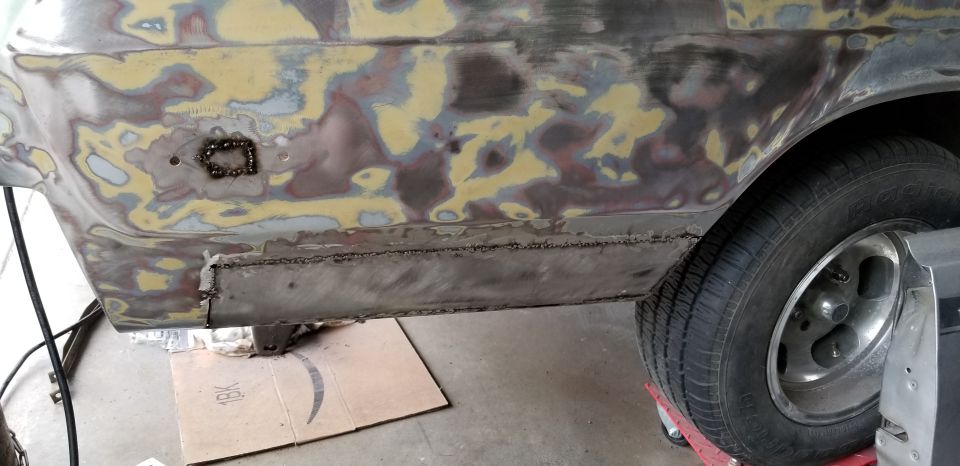 Bare-metal car side showing welded rocker panel patch and grinder marks during bodywork restoration