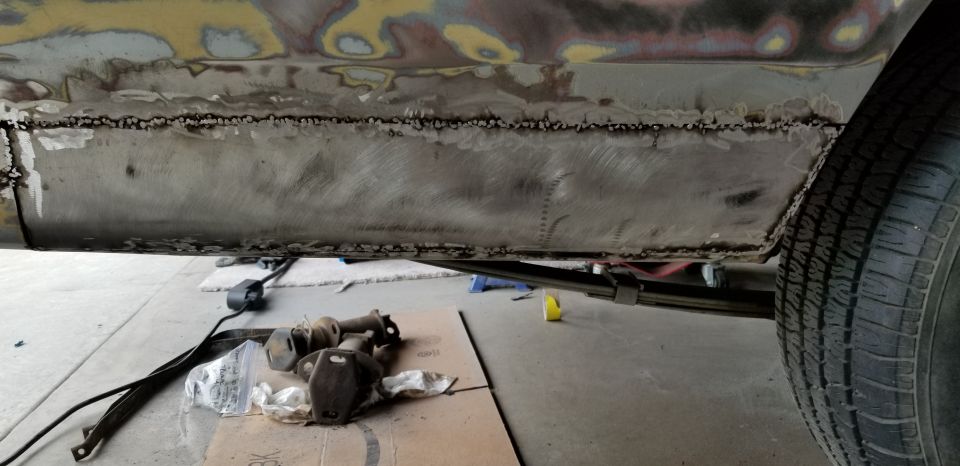 Bare metal rocker panel with welded patch seam on car during bodywork, parts on cardboard below