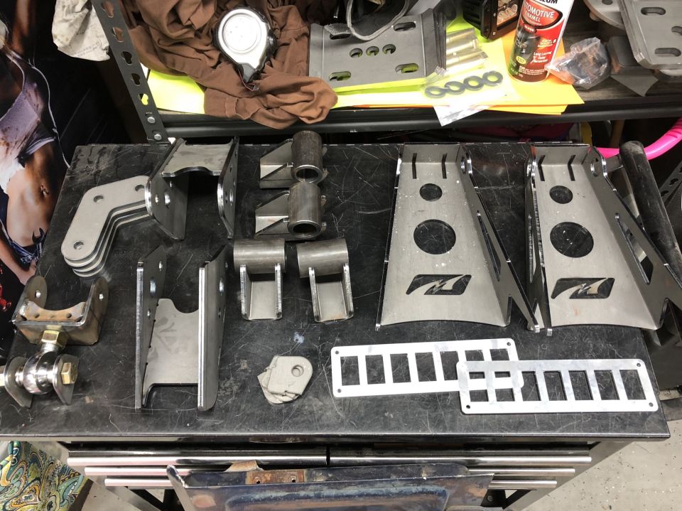 Metal drivetrain parts laid out on a workbench, including brackets and suspension components