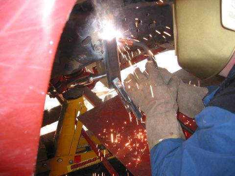 1985 Ford Bronco - A person welds a vehicle frame, with sparks flying and a jack stand visible.