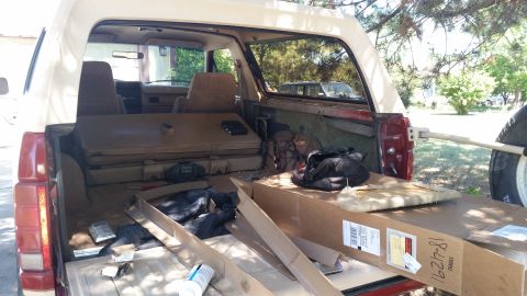 1985 Ford Bronco - The interior of a vintage SUV shows a cluttered cargo area with boxes and bags, and a spare tire mounted externally.