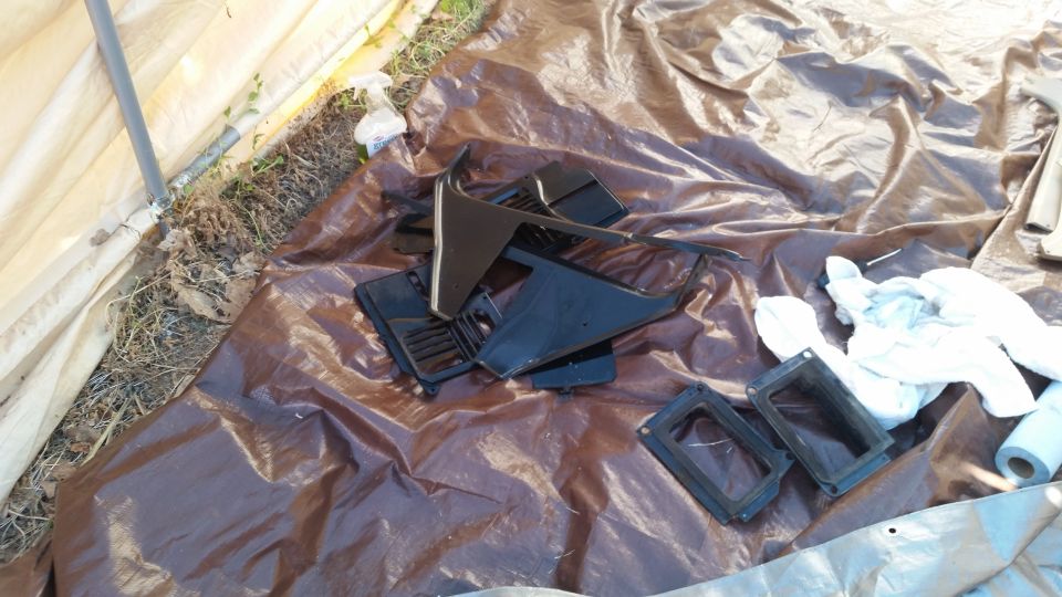 Black plastic dashboard trim pieces and air vents laid out on a brown tarp