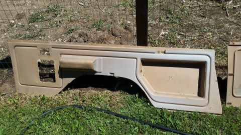 1985 Ford Bronco - Two tan interior door panels are shown lying on the grass outdoors.