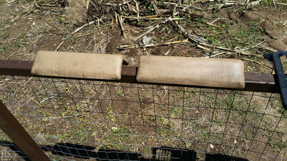 Two tan armrests mounted on a rusty metal bar over a wire fence