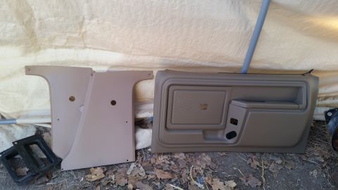 1985 Ford Bronco - Interior trim pieces, including a door panel, are shown laid out on the ground.