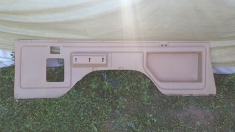 1985 Ford Bronco - This tan interior panel features a wheel well cutout and three key hooks, likely from a vehicle's rear section.