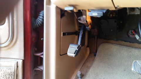 1985 Ford Bronco - Interior view of the driver's side footwell in a vintage Ford Bronco, showing the brake pedal, hood release lever, and part of the door jam…
