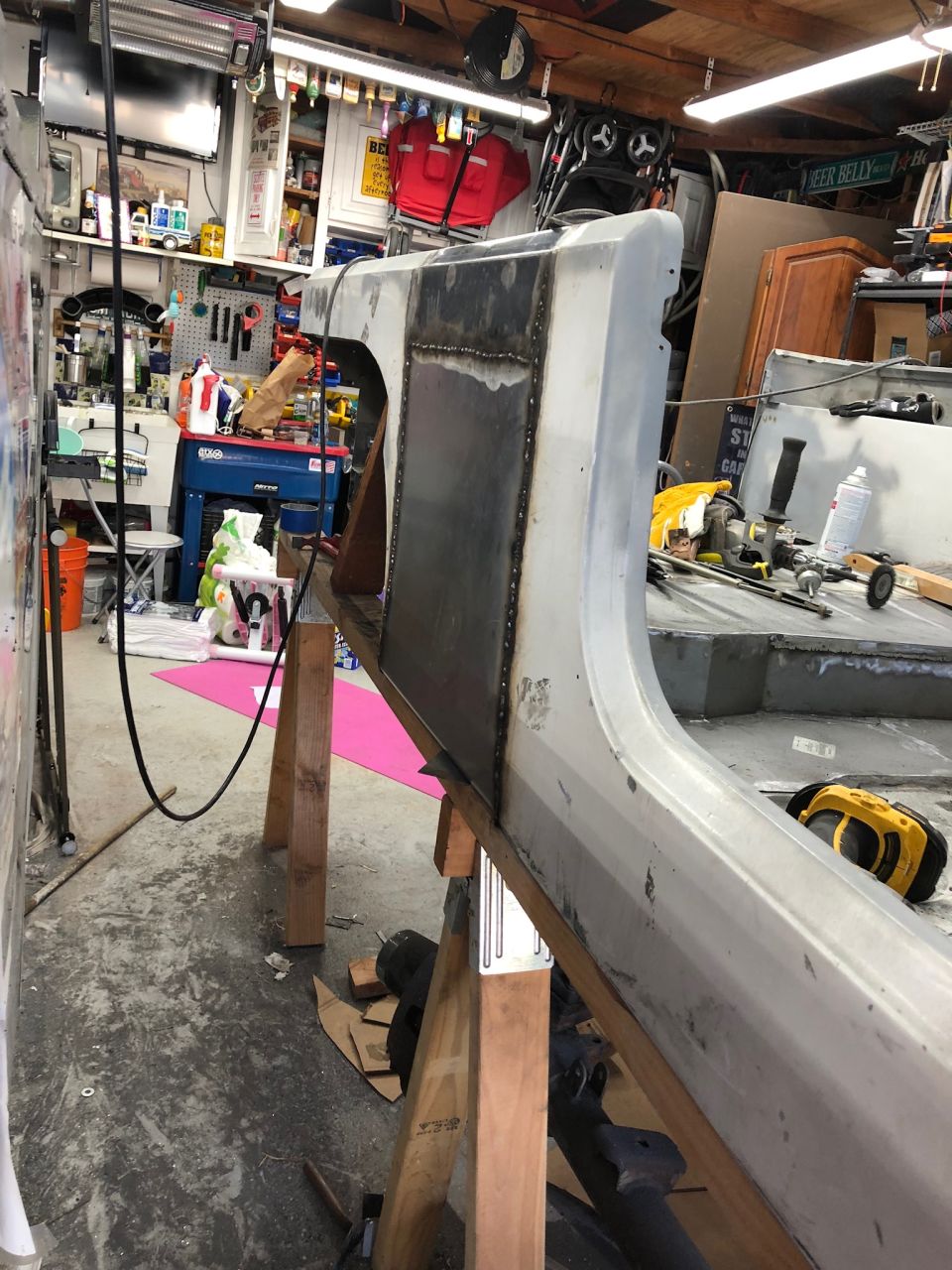 Vehicle body panel with welded repair section on sawhorses in a garage.
