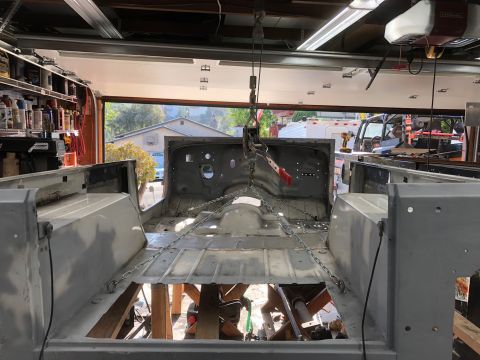 1992 Jeep Wrangler - The bare metal body of a Jeep Wrangler is suspended by chains and a hoist in a garage. The vehicle's interior floor and firewall are visibl…