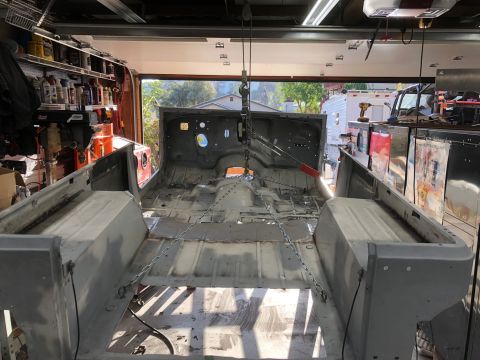 1992 Jeep Wrangler - The bare metal tub of a Jeep Wrangler is suspended by chains and a hoist inside a garage. The interior is stripped down, showing the floor…