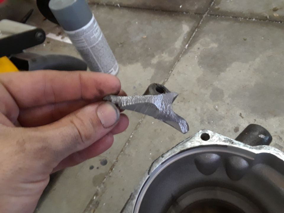 Broken metal engine part held in hand over engine housing