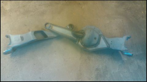 1992 Ford Bronco - A stripped front axle housing with its stamped center section and differential bulge lies on a concrete floor, with a radius arm laid acros…