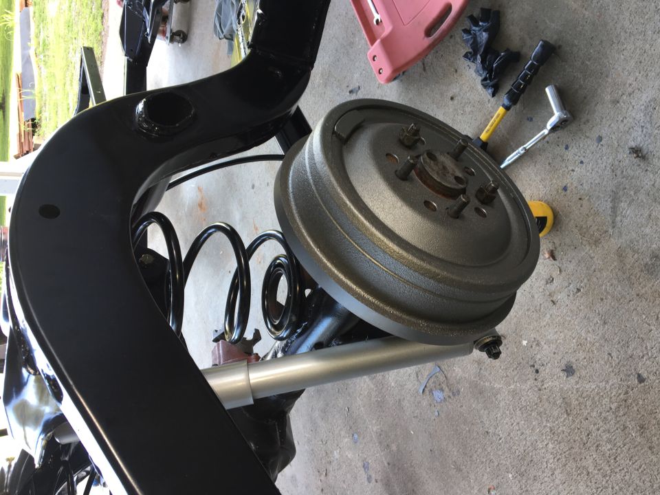 Vehicle rear suspension assembly with black frame, coil spring, and brake drum.