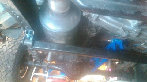 1992 Ford Bronco - The underside of a vehicle, showing the rear axle, suspension components, and exhaust system. A blue aftermarket part is visible attached t…