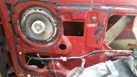 1985 Ford Bronco - The interior of a red vehicle door shows a speaker mounted in the door panel. Wiring and metal structural components are visible behind the…