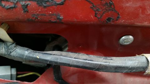 1985 Ford Bronco - A close-up view shows a section of red vehicle body with peeling black paint and a bundle of black electrical wiring secured with tape. A s…