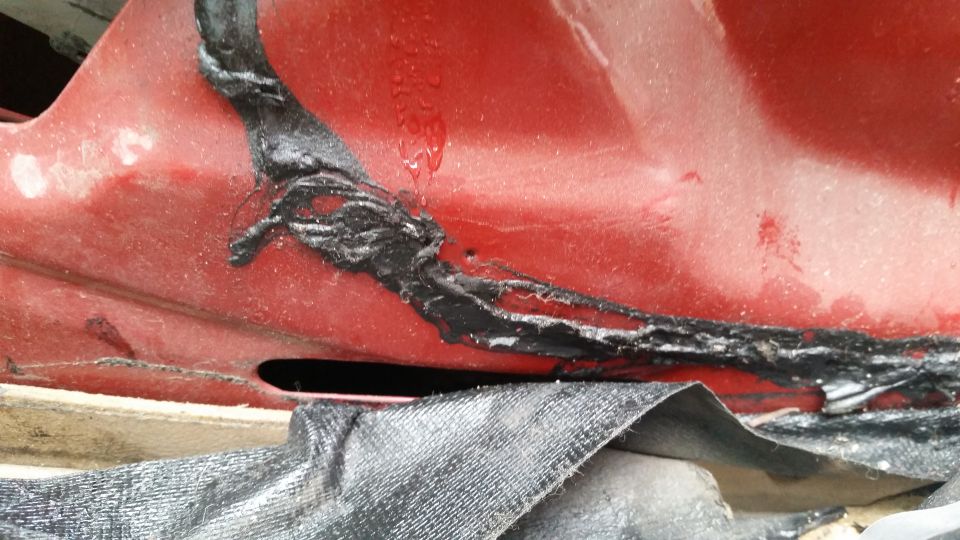 Close-up of red vehicle body with black sealant and black mesh fabric.