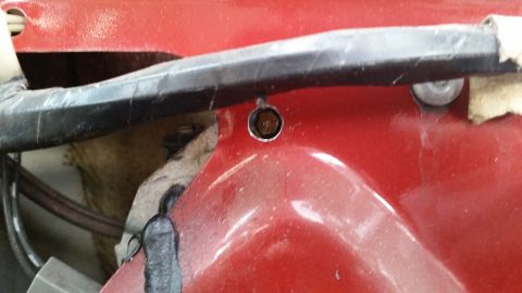 1985 Ford Bronco - A close-up shot shows a bolt securing a black metal bar to a red painted vehicle panel. The bolt head is hexagonal and appears to be brass…