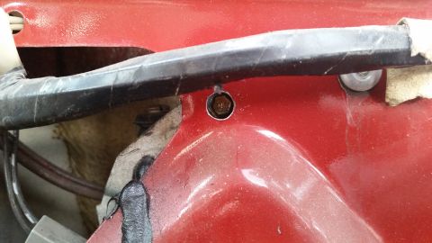 1985 Ford Bronco - A close-up view shows a bolt securing a black plastic trim piece to the red painted body of a vehicle. Wires are visible beneath the trim.