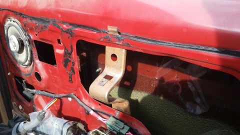 1985 Ford Bronco - This is a close-up view of the interior of a red car door, showing the internal components and wiring. The image reveals a speaker, a metal…
