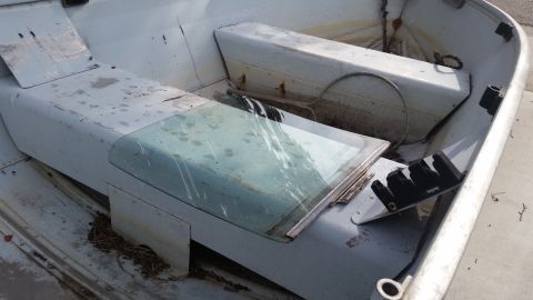 1985 Ford Bronco - The interior of an old, weathered aluminum boat shows two bench seats, a small windshield, and some debris scattered around. One seat has a…