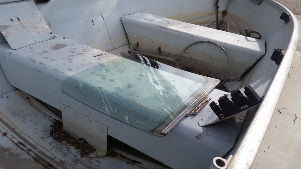 Interior of an old aluminum boat with bench seats and a windshield.