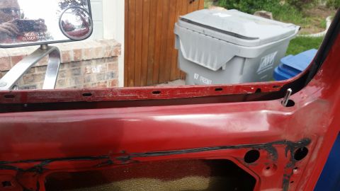1985 Ford Bronco - Close-up view of the red interior door panel of a vehicle, showing mounting holes and a metal pin protruding from the upper section. The ba…