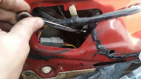 1985 Ford Bronco - A hand uses a wrench to work on wiring inside the red body of a vehicle, near a gray electrical connector.