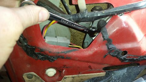 1985 Ford Bronco - A hand uses a Craftsman wrench to tighten a bolt on the red interior panel of a vehicle. Visible wiring and a gray electrical connector are…