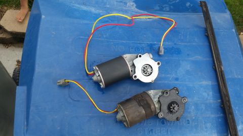 1985 Ford Bronco - Two power window motors with red and yellow wires attached are laid out on a blue surface. A black rubber trim piece is visible to the righ…