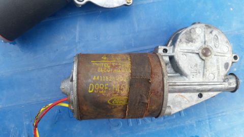 1985 Ford Bronco - A close-up of a rusty, vintage Ford windshield wiper motor with visible yellow and red wires. Text on the motor reads "UNITED TECHNO ELECTR…