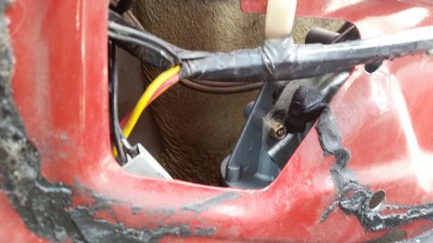 1985 Ford Bronco - Close-up view of the interior of a red vehicle door, showing wiring harnesses, a metal rod, and a gray plastic component attached to the do…
