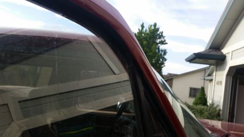 1985 Ford Bronco - Close-up view of the maroon paint and black trim around the windshield of a vehicle, with a residential garage and trees visible in the bac…