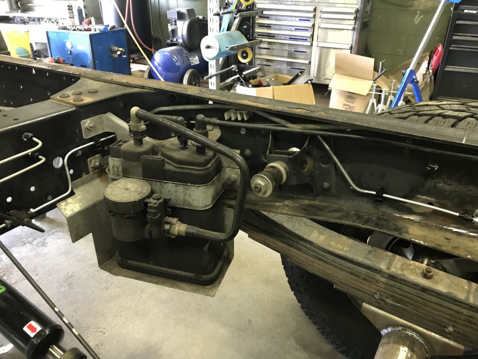 Undercarriage of a truck frame with suspension, brake lines, and a large black component.