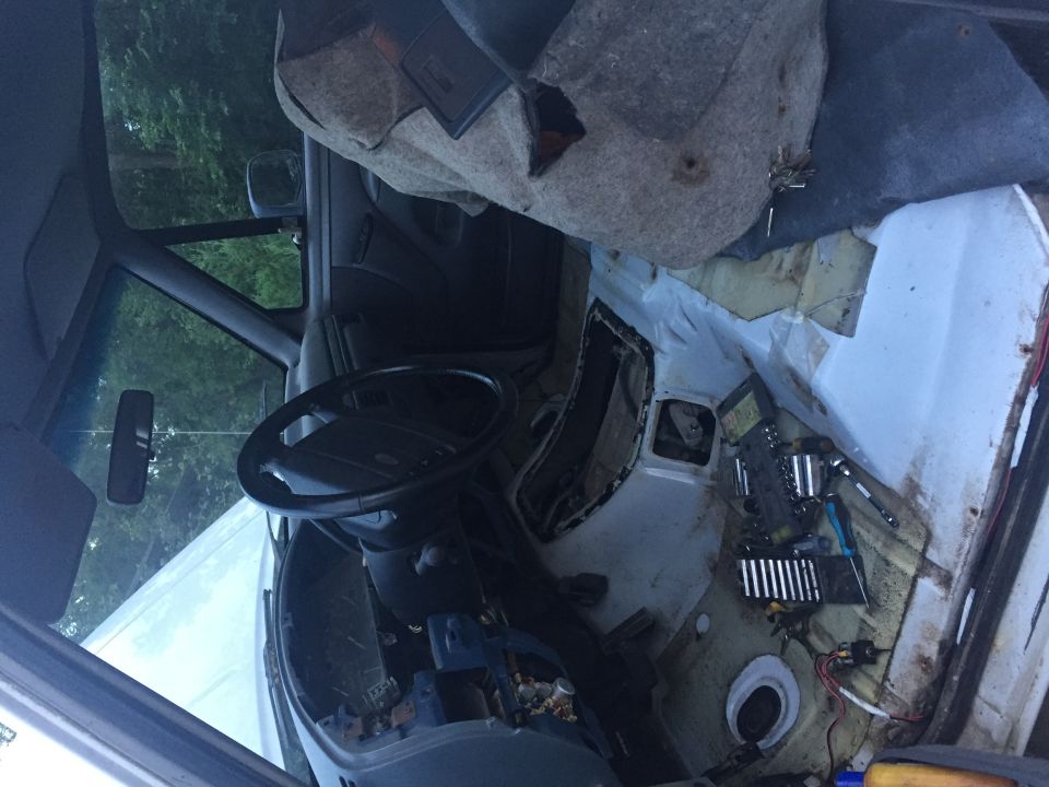 Interior of a vehicle with dashboard and flooring removed, tools on the floor.