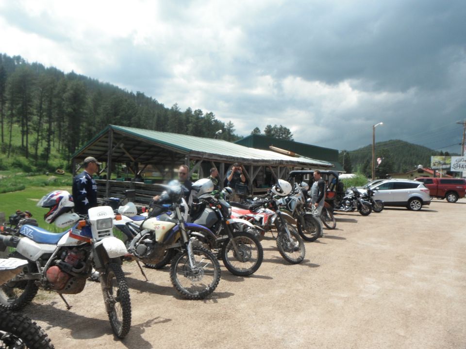 A line of dirt bikes parked on a dirt lot.