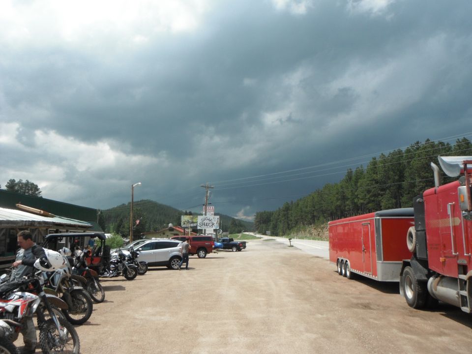 Motorcycles parked in front of a building, with a red semi-truck and trailer on the side of the road.