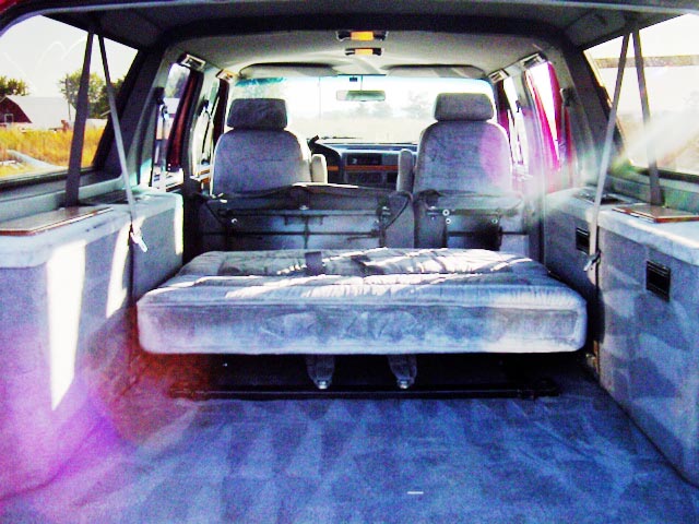 Rear interior of conversion van with folded bench bed and gray captain's chairs