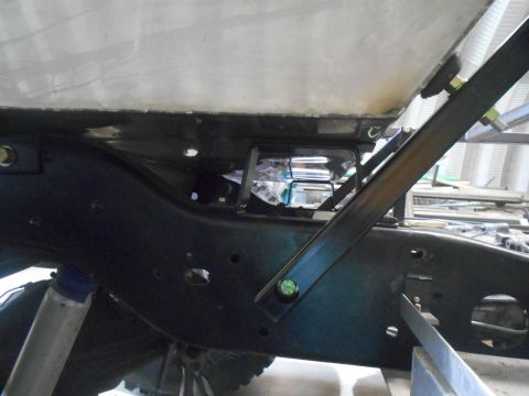 1992 Ford Bronco - A close-up view of the underside of a vehicle frame, showing a metal tank secured with bolts and brackets. A shock absorber is visible at t…