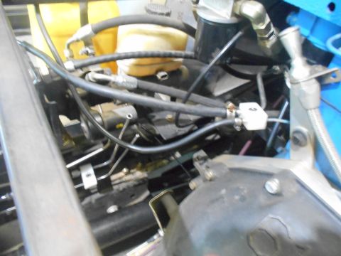 1992 Ford Bronco - A close-up view of the engine bay of a vehicle, showing various hoses, fluid reservoirs, and mechanical components. A yellow fluid reservoi…