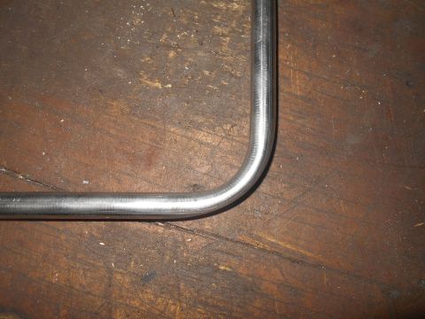 1992 Ford Bronco - A bent metal pipe rests on a weathered wooden surface. The pipe has a smooth, metallic finish and is curved at a right angle.