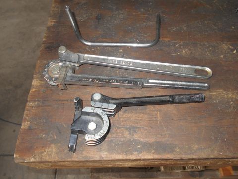 1992 Ford Bronco - Three tube benders of different sizes are laid out on a wooden workbench. A bent metal tube is also visible.