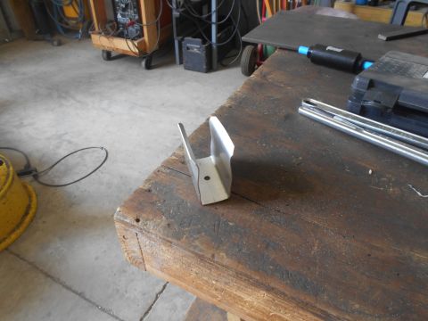 1992 Ford Bronco - A metal bracket with a single hole is shown on a wooden workbench. In the background, a welding machine and other tools are visible in a wo…