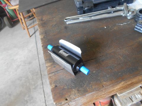 1992 Ford Bronco - A black fuel filter with blue ends and a silver bracket is shown resting on a wooden workbench. The filter has the word "Summit" printed on…