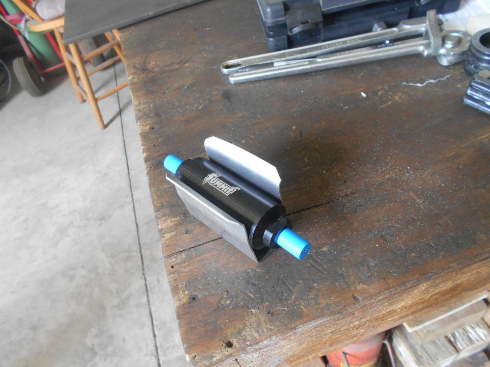 Black Summit fuel filter with blue ends in a silver bracket on a wooden workbench.