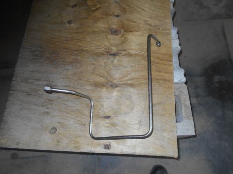 1992 Ford Bronco - A bent metal tube with fittings on each end rests on a piece of plywood. The plywood is on top of concrete blocks.