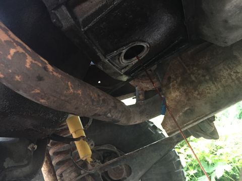 1996 Ford Bronco - Underside view of a vehicle, showing the exhaust pipe and a dipstick being used to check fluid levels. The vehicle appears to be an older m…