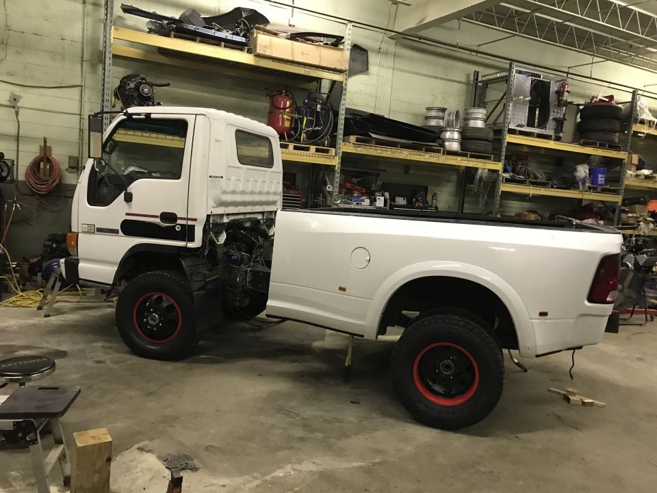 White custom pickup truck with off-road tires and red rim accents in a garage.