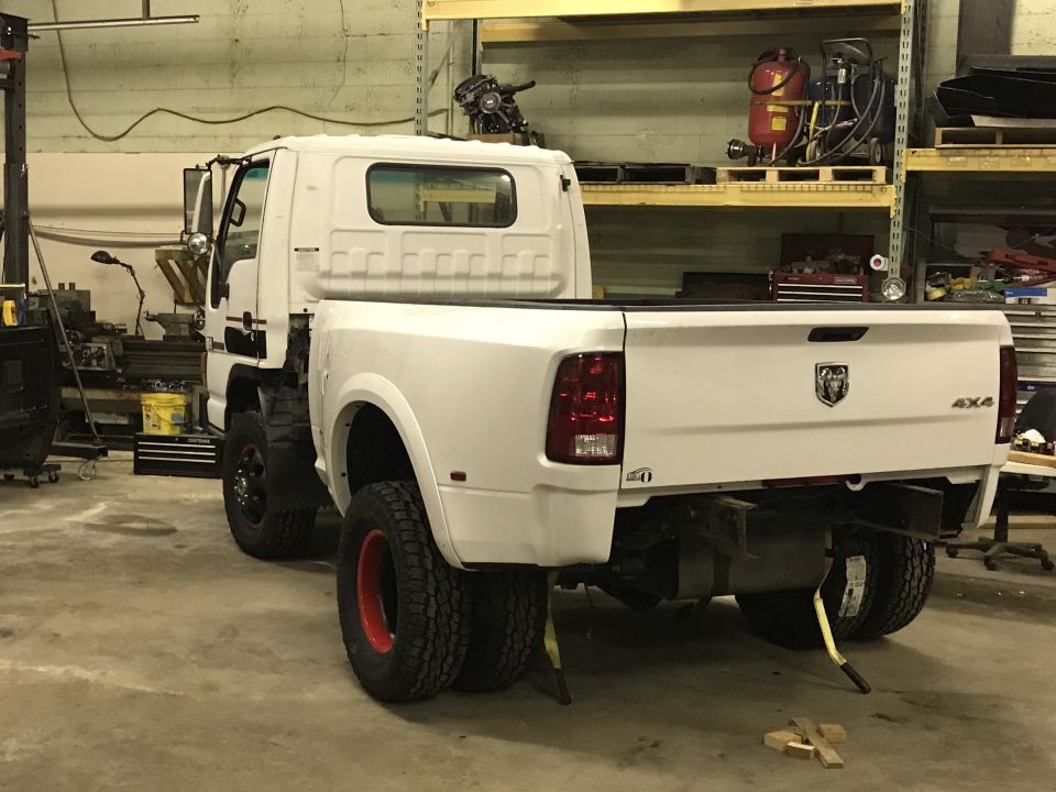 White pickup truck chassis with a different cab, parked in a workshop, rear view.