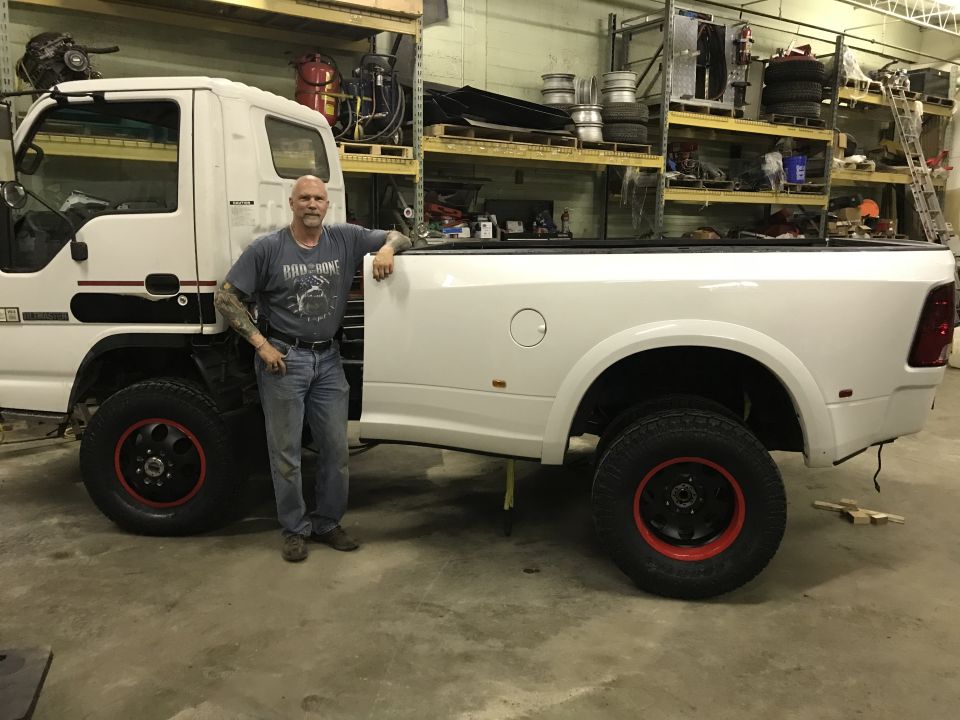 Man standing next to a custom white pickup truck with large black wheels with red accents.